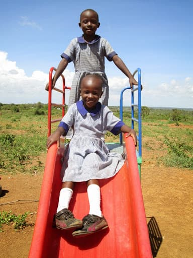 Two children in school uniform on a red plastic slide